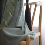 Rideau élégant de couleur vert pâle drapé sur une chaise en bois stylée, accompagné d'un vase décoratif noir contemporain. Scène d'intérieur moderne et minimaliste, parfaite pour ajouter une touche de sophistication et de fraîcheur à votre salon. Accessoire idéal pour une ambiance chaleureuse et naturelle.