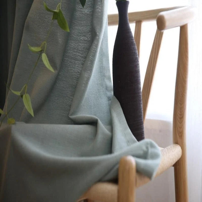 Rideau élégant de couleur vert pâle drapé sur une chaise en bois stylée, accompagné d'un vase décoratif noir contemporain. Scène d'intérieur moderne et minimaliste, parfaite pour ajouter une touche de sophistication et de fraîcheur à votre salon. Accessoire idéal pour une ambiance chaleureuse et naturelle.