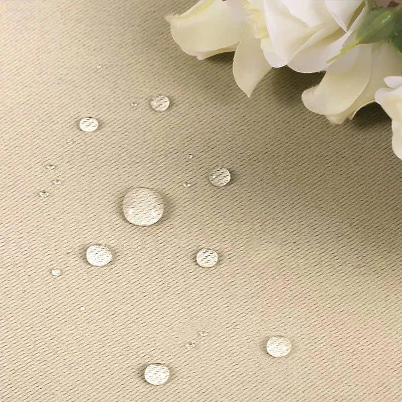 Gouttelettes d'eau sur un tissu beige adorné de fleurs blanches, illustrant la résistance à l'eau et l'élégance du produit. Idéal pour les décorations intérieures raffinées et pratiques, assurant protection et style.
