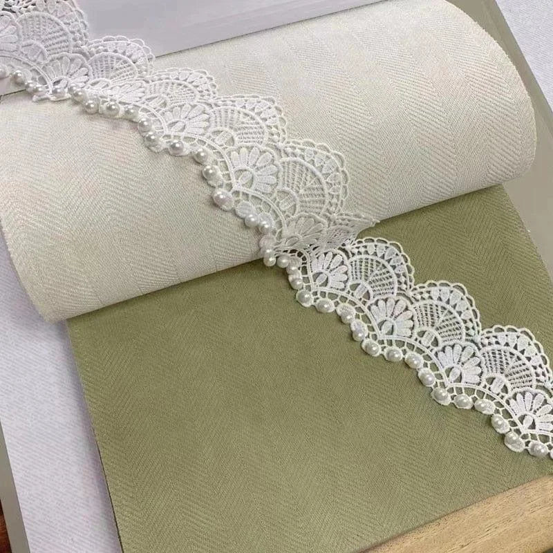 Rouleau de tissu beige agrémenté de dentelle blanche délicate et ornée de perles, parfait pour la décoration intérieure et les projets de couture créatifs. Idéal pour ajouter une touche élégante et raffinée à vos créations maison ou vos événements spéciaux.