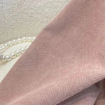 Étoffe élégante de couleur rose pâle avec motif à chevrons subtil, parfaite pour la confection de vêtements raffinés. Accessoire de mode idéal pour une touche de sophistication.