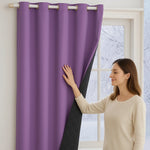 Femme touchant un rideau thermique violet doublé de tissu matelassé noir, suspendu à une tringle à œillets devant une fenêtre hivernale.