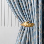 Attache-rideau élégant en forme de main en or, ajoutant une touche artistique et sophistiquée à un rideau bleu à motifs. Accessoire de décoration d'intérieur design pour sublimer votre espace de vie avec originalité.