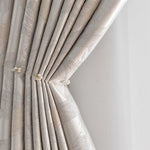 Rideau élégant beige clair avec un motif floral délicat, rehaussé par une embrasse décorative ornée de perles, ajouté pour un style raffiné dans tout intérieur moderne. Idéal pour embellir un salon ou une chambre à coucher, ce rideau est un choix parfait pour ceux cherchant une touche de sophistication. Adapté aussi bien aux décors contemporains qu'aux styles classiques, il offre une solution esthétique et pratique pour la gestion de la lumière naturelle.