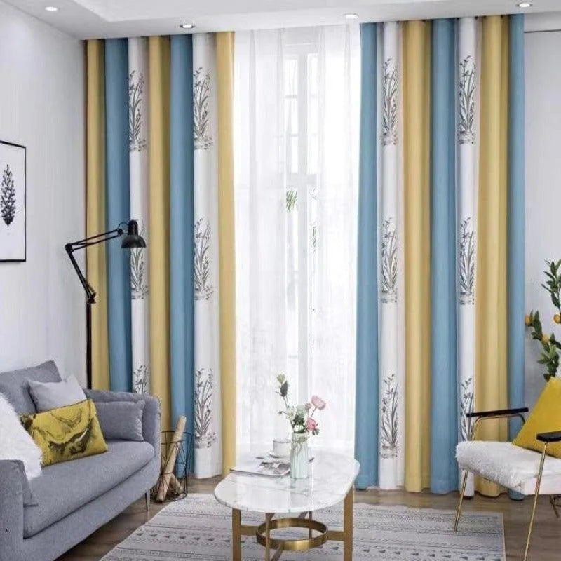 Salon moderne avec rideaux à motifs floraux, combinant des teintes de bleu et de jaune. Canapé gris confortable, décoré avec des coussins assortis, table basse élégante et lampe noire design. Ambiance lumineuse et accueillante, idéale pour un espace de vie contemporain.