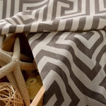 Tissu décoratif à motifs géométriques zigzag gris et blanc, idéal pour la décoration d'intérieur moderne. Parfait pour créer une ambiance élégante et sophistiquée. Accessoires marins en arrière-plan ajoutant une touche de bord de mer.