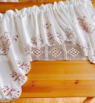 Rideau blanc décoratif avec motifs floraux brodés et détail ajouré, idéal pour ajouter une touche d’élégance à votre cuisine ou salon. Design raffiné et charme authentique pour illuminer vos espaces intérieurs avec style.