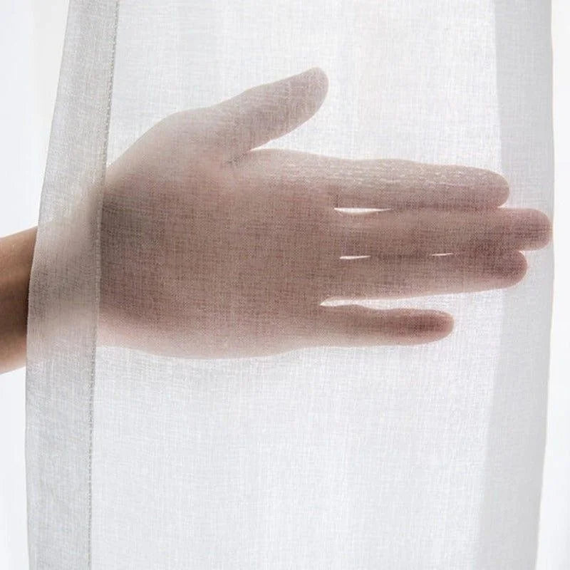 Main derrière un voilage transparent blanc pour la décoration intérieure, idéal pour tamiser la lumière dans le salon ou la chambre avec élégance. Solution pratique et esthétique pour les fenêtres.