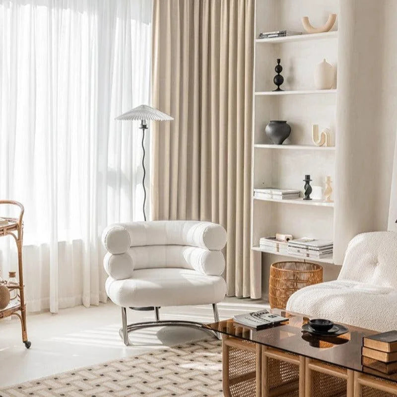 Fauteuil design moderne blanc dans un salon élégant et lumineux. Aménagement intérieur avec des éléments décoratifs contemporains, des rideaux beiges et une étagère minimaliste. Ambiance chaleureuse et sophistiquée pour un espace de vie accueillant.