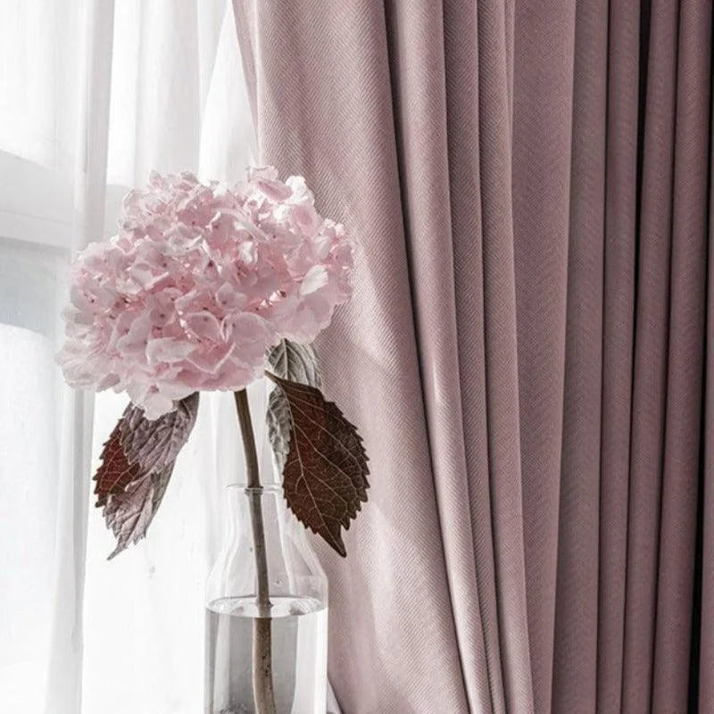 Image d'un vase en verre contenant une fleur rose délicate, placé devant des rideaux élégants de couleur rose pâle. L'ensemble crée une atmosphère douce et accueillante, idéale pour une décoration intérieure raffinée et apaisante. Le contraste entre la transparence du vase et la texture des rideaux ajoute une touche de sophistication.
