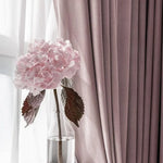 Image d'un vase en verre contenant une fleur rose délicate, placé devant des rideaux élégants de couleur rose pâle. L'ensemble crée une atmosphère douce et accueillante, idéale pour une décoration intérieure raffinée et apaisante. Le contraste entre la transparence du vase et la texture des rideaux ajoute une touche de sophistication.