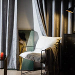 Chaise moderne avec coussin blanc dans un coin détente intérieur, entourée de rideaux élégants. À côté, un tableau artistique ajoute une touche de caractère à la décoration. Éclairage tamisé pour une ambiance cosy et sophistiquée.