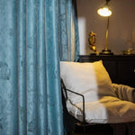 Rideaux bleus élégants pour salon, créant une ambiance chaleureuse et moderne. Le fauteuil confortable accentue un espace de détente idéal, rehaussé par un éclairage doux provenant d'une lampe design. Parfaite combinaison pour une décoration intérieure harmonieuse.