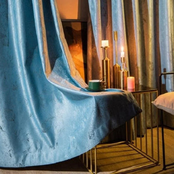 Rideau bleu élégant dans un environnement intérieur chaleureux, avec une table d'appoint décorée de bougies et d'une tasse verte, créant une ambiance apaisante et sophistiquée. Décoration de chambre moderne et luxueuse.
