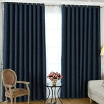 Rideau occultant bleu foncé élégant dans un salon moderne, monté sur une tringle à œillets. Le rideau ajoute une touche sophistiquée à la décoration intérieure, complétant un fauteuil vintage en bois et un lampadaire. Solution idéale pour une ambiance chaleureuse et intimiste.