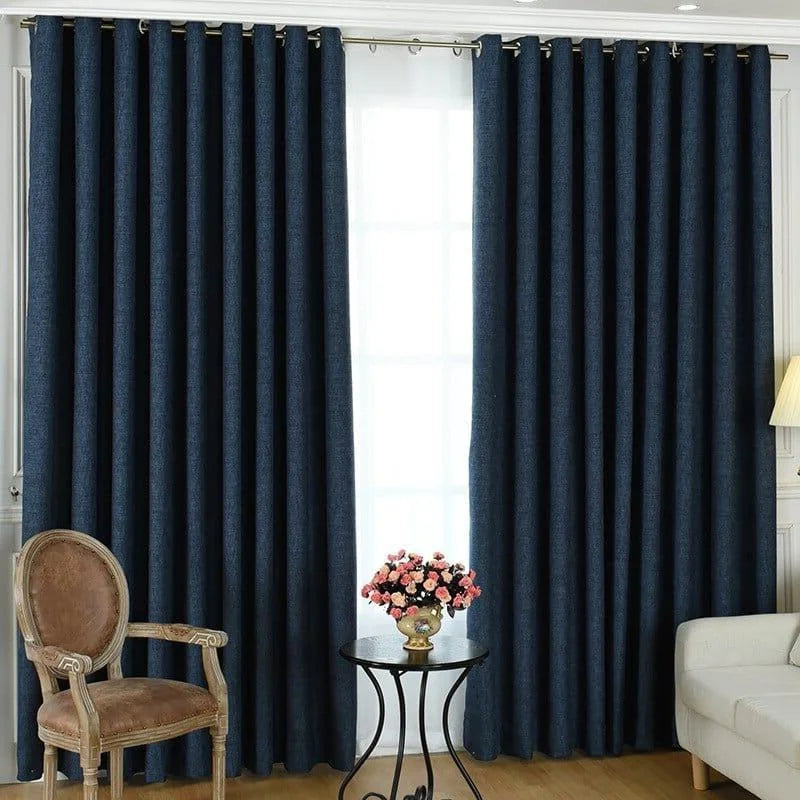 Rideau occultant bleu foncé élégant dans un salon moderne, monté sur une tringle à œillets. Le rideau ajoute une touche sophistiquée à la décoration intérieure, complétant un fauteuil vintage en bois et un lampadaire. Solution idéale pour une ambiance chaleureuse et intimiste.