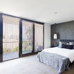 Chambre moderne avec lit confortable et rideaux décoratifs. Une grande baie vitrée laisse entrer la lumière naturelle, accentuant le style élégant et épuré de l'intérieur. Le mur sombre souligne le contraste avec le linge de lit clair et les coussins décoratifs. Idéal pour créer une ambiance sereine et contemporaine.