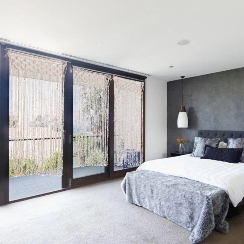 Chambre moderne avec lit confortable et rideaux décoratifs. Une grande baie vitrée laisse entrer la lumière naturelle, accentuant le style élégant et épuré de l'intérieur. Le mur sombre souligne le contraste avec le linge de lit clair et les coussins décoratifs. Idéal pour créer une ambiance sereine et contemporaine.