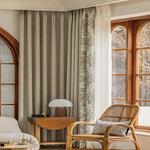 Rideaux élégants pour salon, ambiance chaleureuse avec voilage décoratif floral, fauteuil en osier, table en bois design et lampe moderne, coin lecture lumineux, décoration intérieure élégante, grandes fenêtres en bois, style contemporain et confortable.