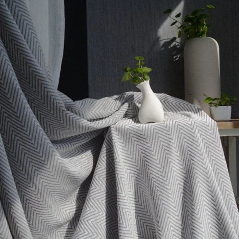 Rideau élégant à motifs chevrons gris et blanc, drapé devant une fenêtre, avec une décoration contemporaine. Idéal pour ajouter une touche de sophistication et de style moderne à n'importe quelle pièce. Composition en tissu de haute qualité, offrant un effet d'ombrage efficace. Accessoire de décoration intérieure, parfait pour salon, chambre ou bureau.