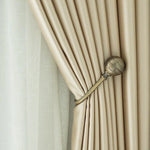 Rideau élégant beige attaché par un embrasse métallique, offrant une décoration raffinée et une lumière tamisée dans la pièce. Design moderne et chic parfait pour une ambiance cosy et contemporaine. Accessoire idéal pour ajouter une touche de sophistication à votre intérieur.