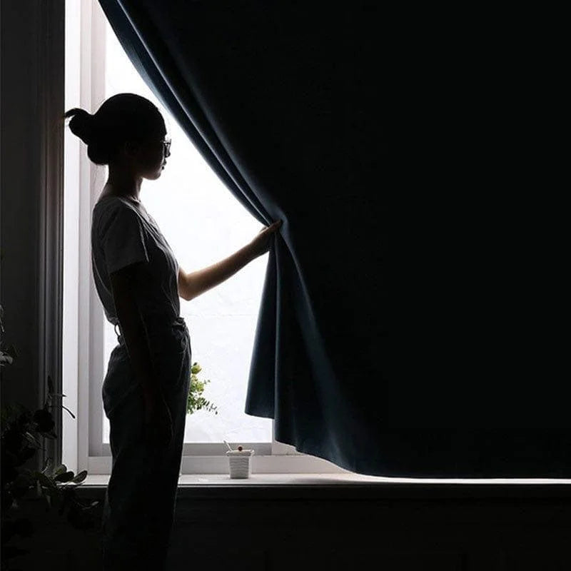 Personne ajustant un rideau épais dans un intérieur lumineux, idéal pour bloquer la lumière et préserver l'intimité. Solution parfaite pour chambre et salon, le rideau foncé accentue la décoration tout en offrant confort et tranquillité.