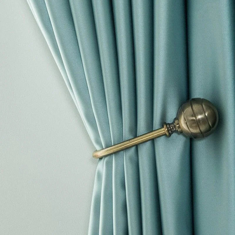 Rideau élégant de couleur turquoise avec embrasse décorative en métal doré. Idéal pour ajouter une touche sophistiquée à votre intérieur, ce design raffiné offre une solution chic pour habiller vos fenêtres. Parfait pour le salon, la chambre ou le bureau, ce rideau apporte une ambiance moderne et apaisante à la pièce.