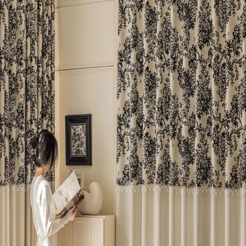 Rideaux élégants à motifs floraux noirs, apportant une touche sophistiquée à un intérieur moderne et chaleureux. Une femme lisant un livre ajoute une ambiance paisible et cosy à la pièce, parfaite pour créer un espace de détente et de confort. Décoration murale assortie, complétant harmonieusement le design de la pièce.