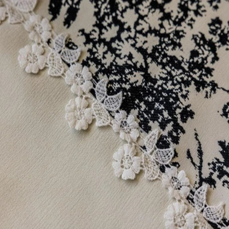 Image d’un tissu élégant avec une bordure en dentelle délicate et un motif graphique noir sur fond blanc, parfait pour la décoration intérieure ou la confection de vêtements raffinés.