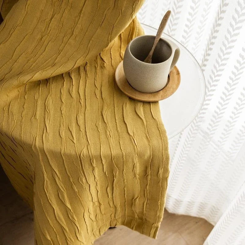 Image montrant un joli rideau jaune texturé drapé sur une table ronde transparente, à côté d'une tasse en céramique beige sur un sous-verre en bois, créant une ambiance apaisante et élégante pour un intérieur chaleureux.