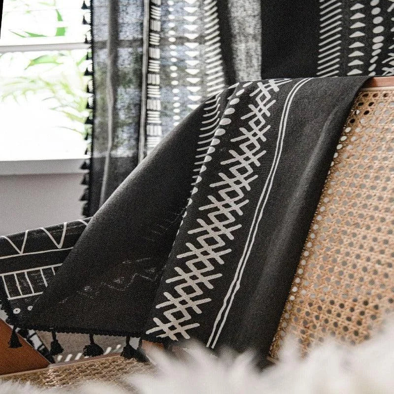 Plaid noir et blanc avec motifs géométriques élégants, posé sur un fauteuil en rotin dans un intérieur lumineux. Idéal pour rehausser votre décoration avec une touche moderne et sophistiquée. Parfait pour sublimer le salon ou la chambre à coucher avec style et confort. Proposez-vous une ambiance chaleureuse et accueillante grâce à cet accessoire déco tendance.
