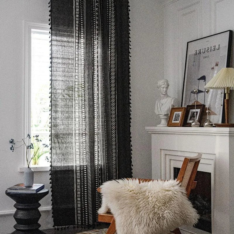 Rideau noir à motifs géométriques suspendu dans un salon élégant. Ce rideau ajoute une touche contemporaine et élégante à la pièce, jouant avec la lumière naturelle provenant de la fenêtre adjacente. Le design est complété par des éléments décoratifs comme une statue et des cadres photo au-dessus de la cheminée, créant une atmosphère harmonieuse et accueillante. Parfait pour un intérieur moderne et sophistiqué.
