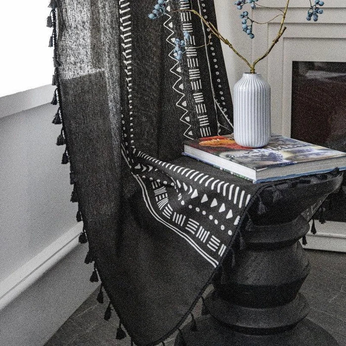 Plaid noir aux motifs géométriques blancs, idéal pour une décoration moderne et élégante. Parfait pour ajouter une touche sophistiquée à votre salon. Vue en situation avec vase et livre, ce plaid rehausse l'ambiance d'une pièce avec style.