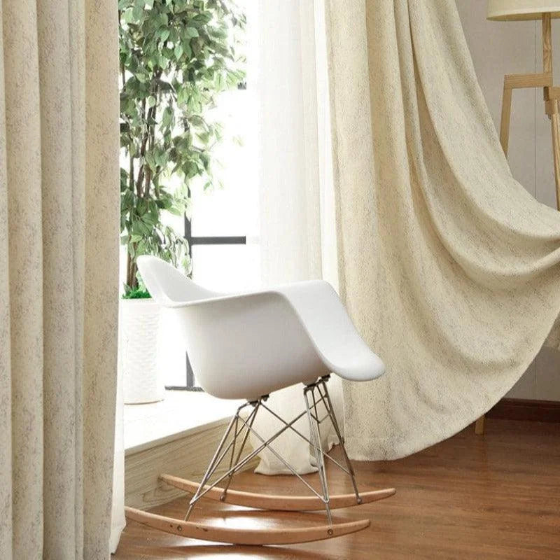 Chaise à bascule design moderne positionnée dans un salon lumineux avec de grandes fenêtres. Idéale pour un intérieur contemporain, elle s'harmonise parfaitement avec des rideaux beiges et un sol en bois clair. Parfaite pour un coin de lecture, cette chaise ajoute une touche élégante et confortable à votre espace de vie.