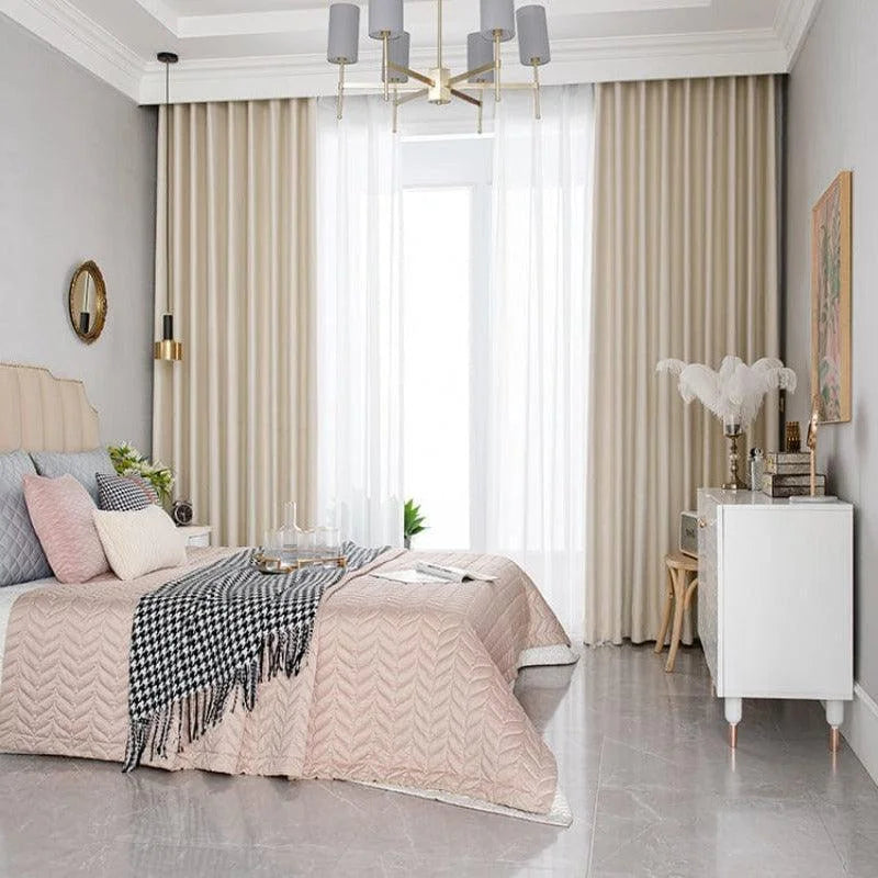 Chambre moderne avec literie élégante et décoration raffinée. Grand lit avec tête de lit rembourrée, draperies longues encadrant une fenêtre pour une ambiance lumineuse. Mobilier chic et accessoires décoratifs, tels que coussins variés et luminaire contemporain, créent un espace paisible et accueillant pour un intérieur stylé et confortable.