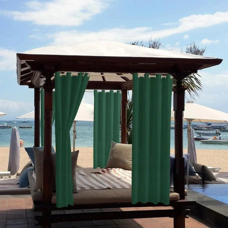 Alt texte : Lit baldaquin extérieur avec rideaux verts sur plage, offrant un espace de détente idéal avec vue sur la mer, sous un ciel bleu. Parfait pour des moments de relaxation sur la terrasse ou au bord de la piscine.
