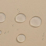 Gros plan sur des gouttes d'eau repoussées sur une surface beige, illustrant l'effet déperlant du produit. Idéal pour démontrer la résistance à l'eau et l'efficacité de la protection contre l'humidité, parfait pour les applications nécessitant une imperméabilité accrue dans des environnements variés.