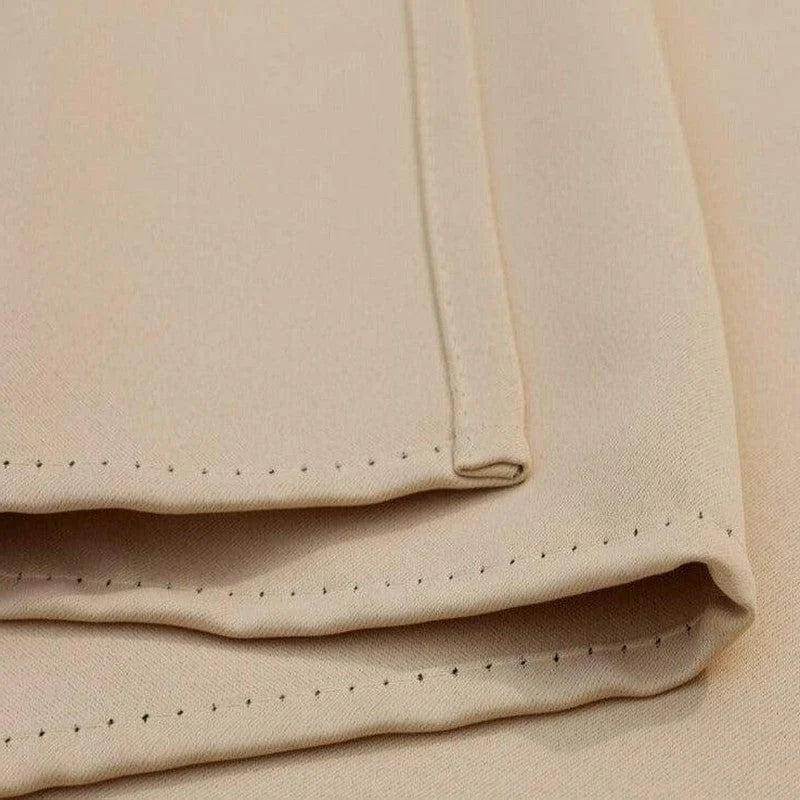 Gros plan sur un tissu beige plié avec une finition soignée et des bords détaillés. L'image montre les coutures précises et le design élégant, idéal pour la confection de vêtements ou de décoration intérieure. Parfait pour les créateurs à la recherche d'un textile de qualité aux lignes épurées et modernes.