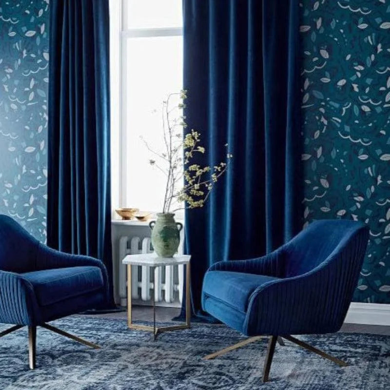 Deux fauteuils bleus élégants dans un intérieur moderne, accompagnés de rideaux assortis et d'un papier peint floral, créent une ambiance chic et apaisante. Le sol est couvert d'un tapis aux motifs subtils, tandis qu'une table d'appoint avec un vase ajoute une touche de verdure à la décoration. Fenêtre lumineuse en arrière-plan apportant clarté et espace à la pièce.