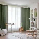 Salon moderne et élégant avec rideaux vert olive, accentuant une ambiance lumineuse et apaisante. Mobilier aux formes arrondies et étagères intégrées apportent une touche contemporaine. Table basse en bois naturel au centre, parfaite pour créer un espace de détente. Idéal pour un intérieur chic et harmonieux.