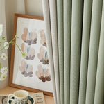 Rideaux élégants vert menthe dans un salon moderne, accompagnés d'un cadre artistique floral et d'une tasse à thé délicatement posée sur une table. Idéal pour ajouter une touche de fraîcheur et de sophistication à votre décoration intérieure.
