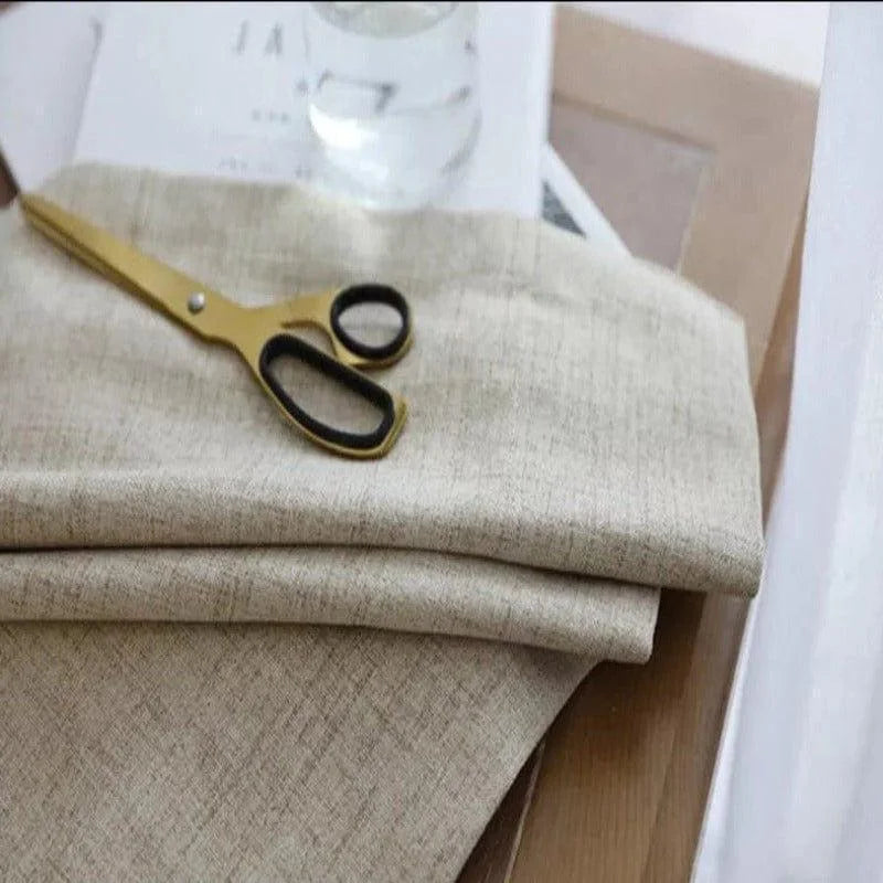 Texte alternatif SEO : Rideau en lin beige doux posé sur une table en bois clair avec une paire de ciseaux dorés. Idéal pour ajouter une touche élégante et naturelle à votre intérieur.