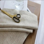 Texte alternatif SEO : Rideau en lin beige doux posé sur une table en bois clair avec une paire de ciseaux dorés. Idéal pour ajouter une touche élégante et naturelle à votre intérieur.