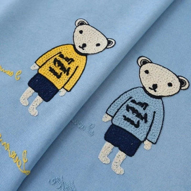 Tissu bleu pour enfant avec motifs brodés d'oursons habillés de pulls colorés et shorts. Cadeau idéal pour vêtements ou accessoires décoratifs dans une thématique amusante et mignonne. Parfait pour créer divers articles personnalisés pour enfants.
