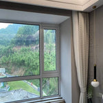Cette image montre une chambre moderne avec une grande fenêtre offrant une vue panoramique sur un paysage verdoyant. Les rideaux élégants ajoutent une touche sophistiquée à l'intérieur, tandis qu'une lampe suspendue au design contemporain illumine l'espace. Idéal pour créer une ambiance lumineuse et apaisante dans votre maison.