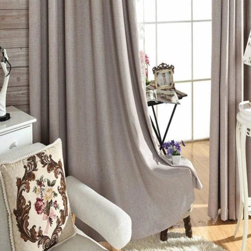 Rideau élégant de couleur neutre dans un salon moderne avec un fauteuil confortable et un coussin décoratif. Ambiance chaleureuse et lumineuse grâce à une grande fenêtre, parfait pour un style intérieur chic.
