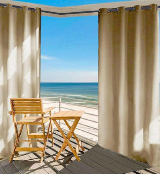Rideau beige pour extérieur avec oeillets sur terrasse en bord de mer, créant un espace ombragé et intime; idéal pour balcons ou patios ensoleillés.