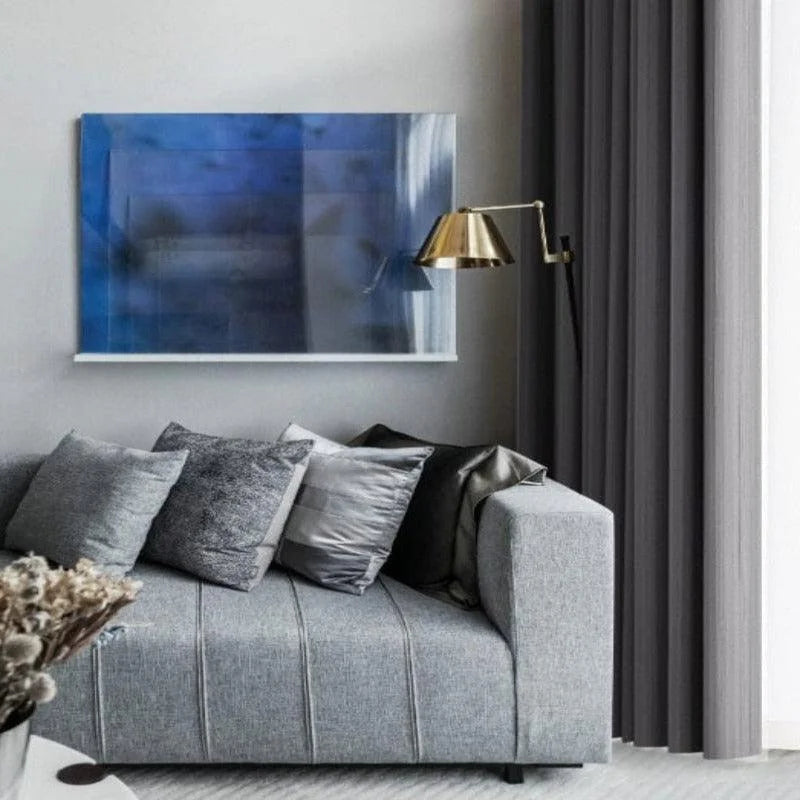 Canapé moderne gris avec coussins variés dans un salon élégant, éclairé par une lampe dorée design. Un tableau abstrait bleu apporte une touche artistique à la décoration intérieure sophistiquée.