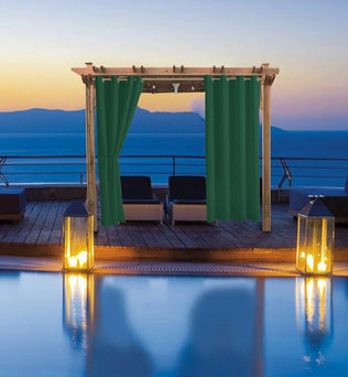 Pergola avec rideaux vert foncé sur terrasse élégante avec vue sur mer au coucher du soleil. Éclairage romantique et ambiance détente autour de la piscine, idéale pour les soirées extérieures. Aménagement extérieur sophistiqué pour jardin ou terrasse, alliant confort et esthétique.