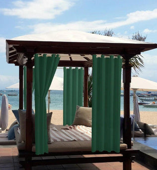 Pergola extérieure sur une plage, équipée de rideaux verts et d'un lit confortable avec des coussins. Idéale pour créer un espace de détente ombragé face à la mer. Accessoire parfait pour jardin ou espace piscine, offrant intimité et style.